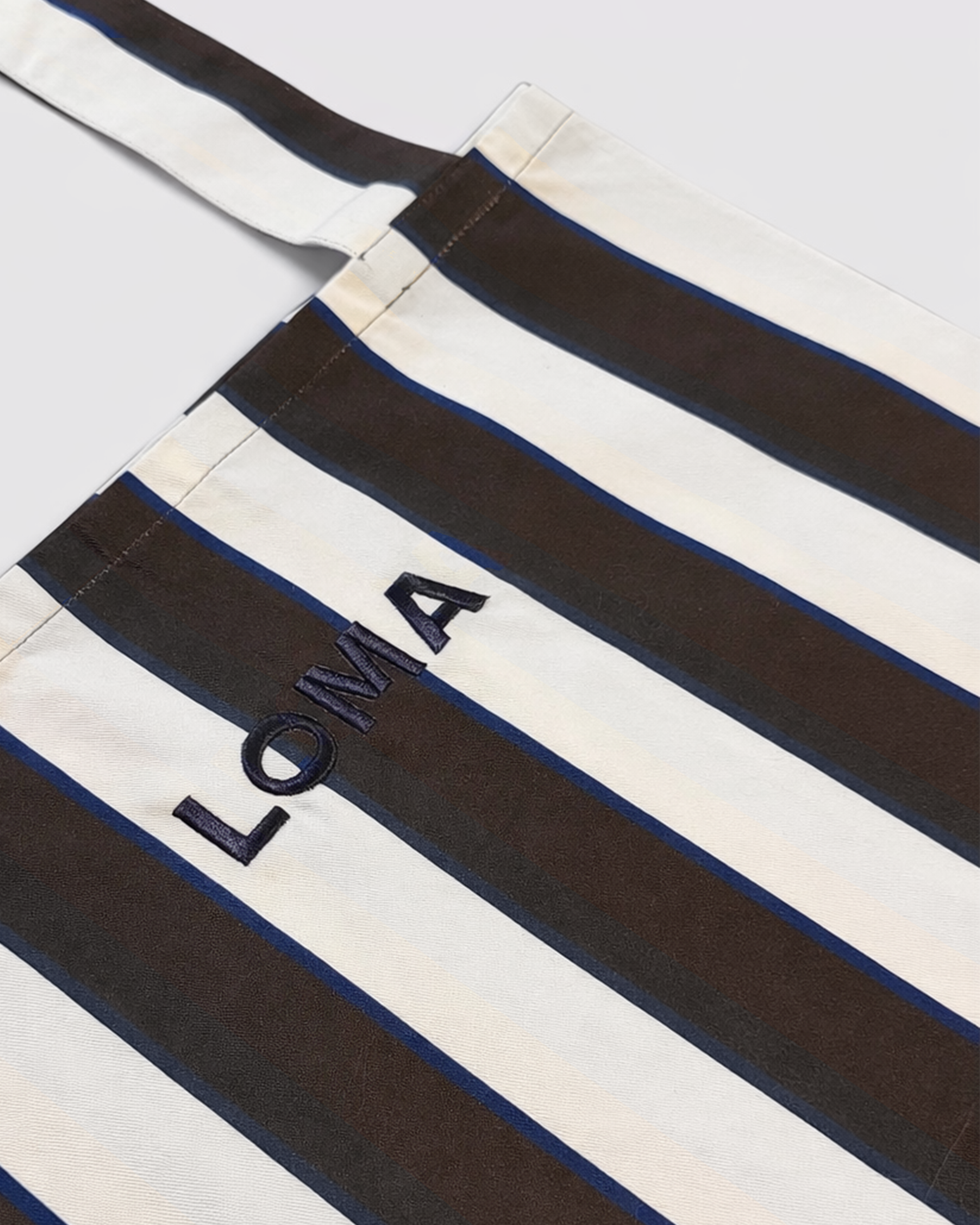 Close up on striped cotton apron in chocolate brown and white with LOMA's logo embroidered in navy blue front view