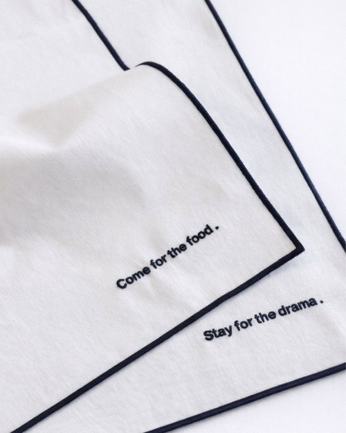 Close up of two white napkins with embroidered navy blue quotes front view