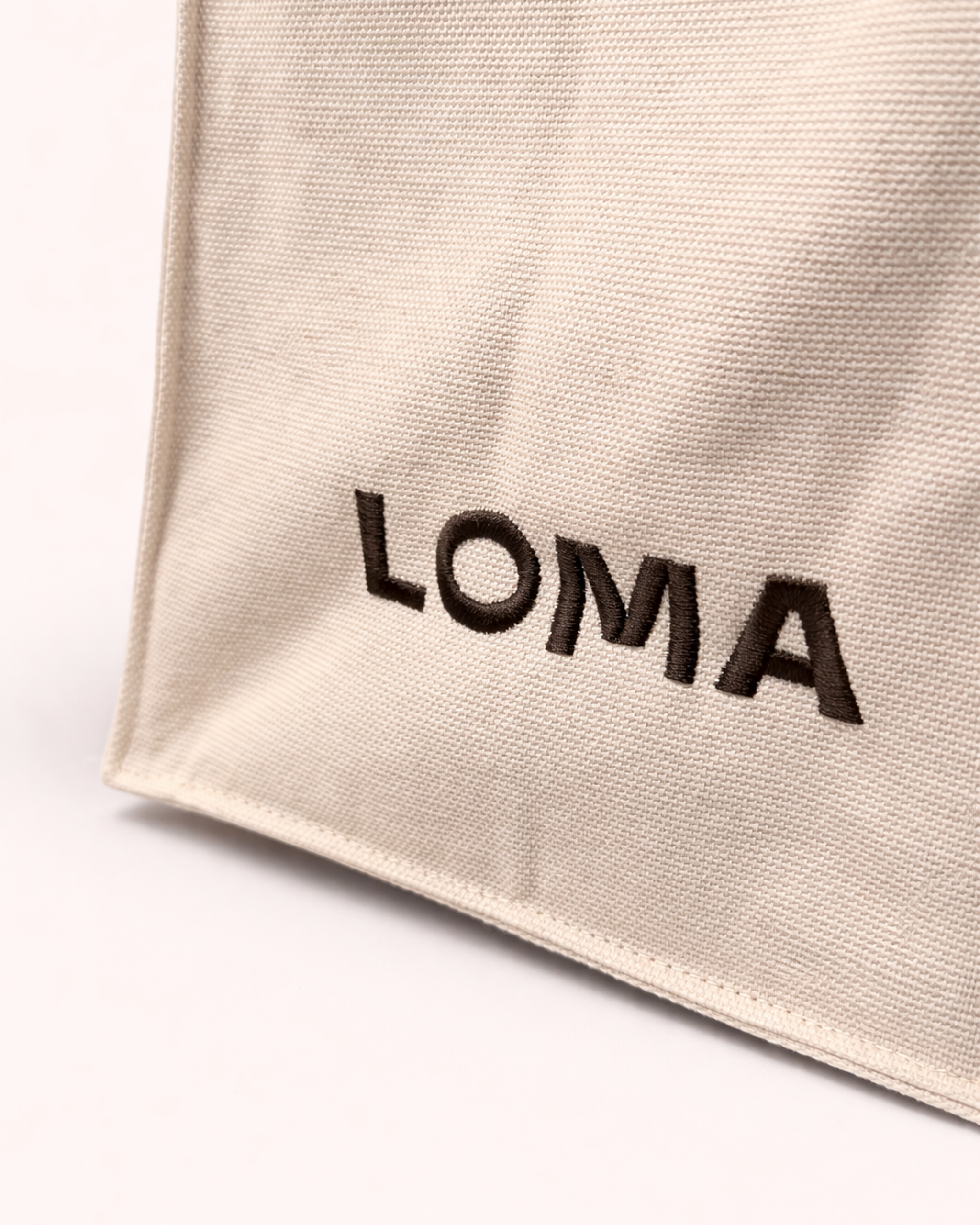Close up of cotton tote bag with LOMA's logo embroidered in chocolate brown side view