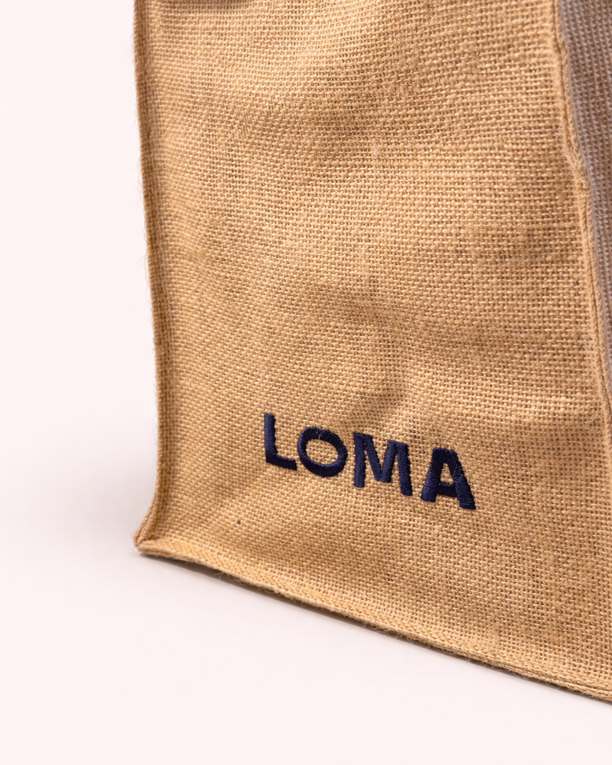 Close up of jute tote bag with LOMA's logo embroidered in navy blue side view